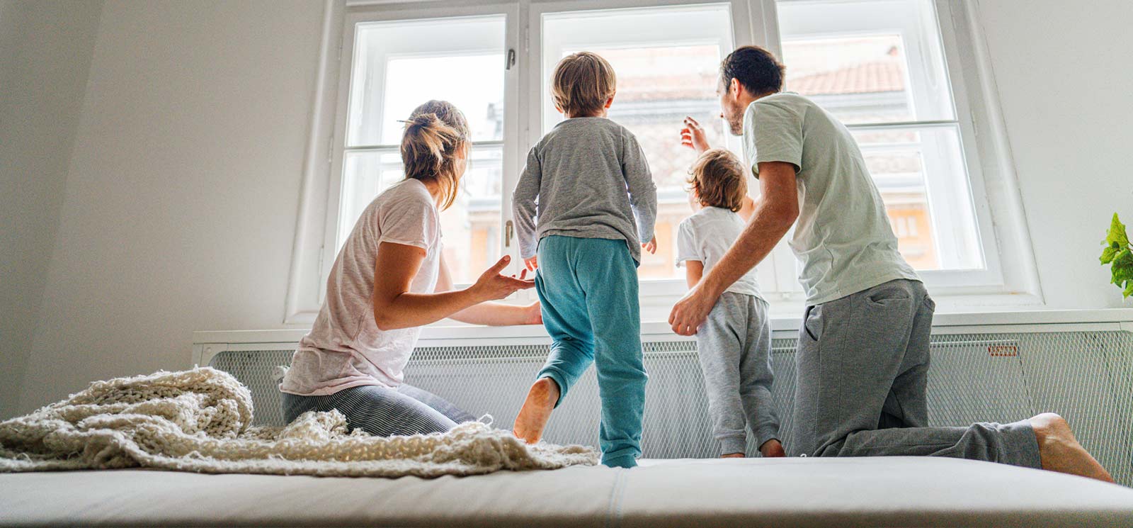 Family standing on the bed and looking out the window.