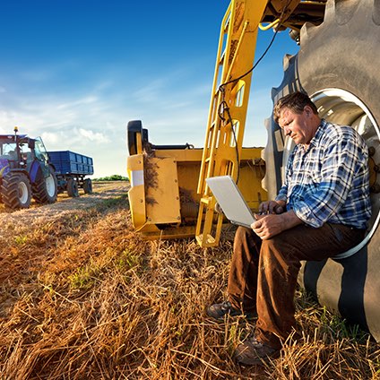 Farmer sitting in a large equipment tire on his laptop.