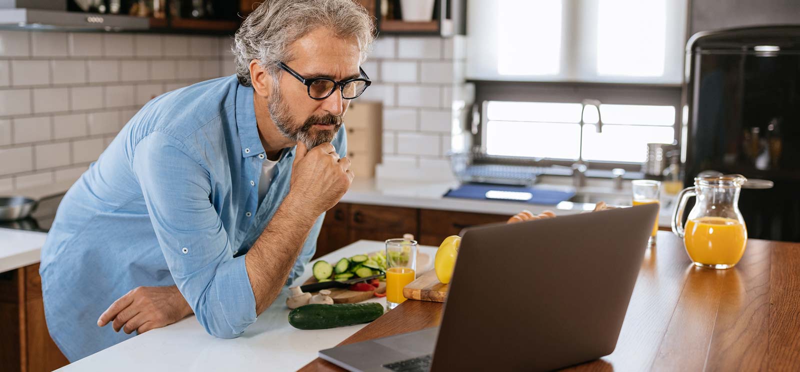 Person standing in kitchen looking at his laptop.