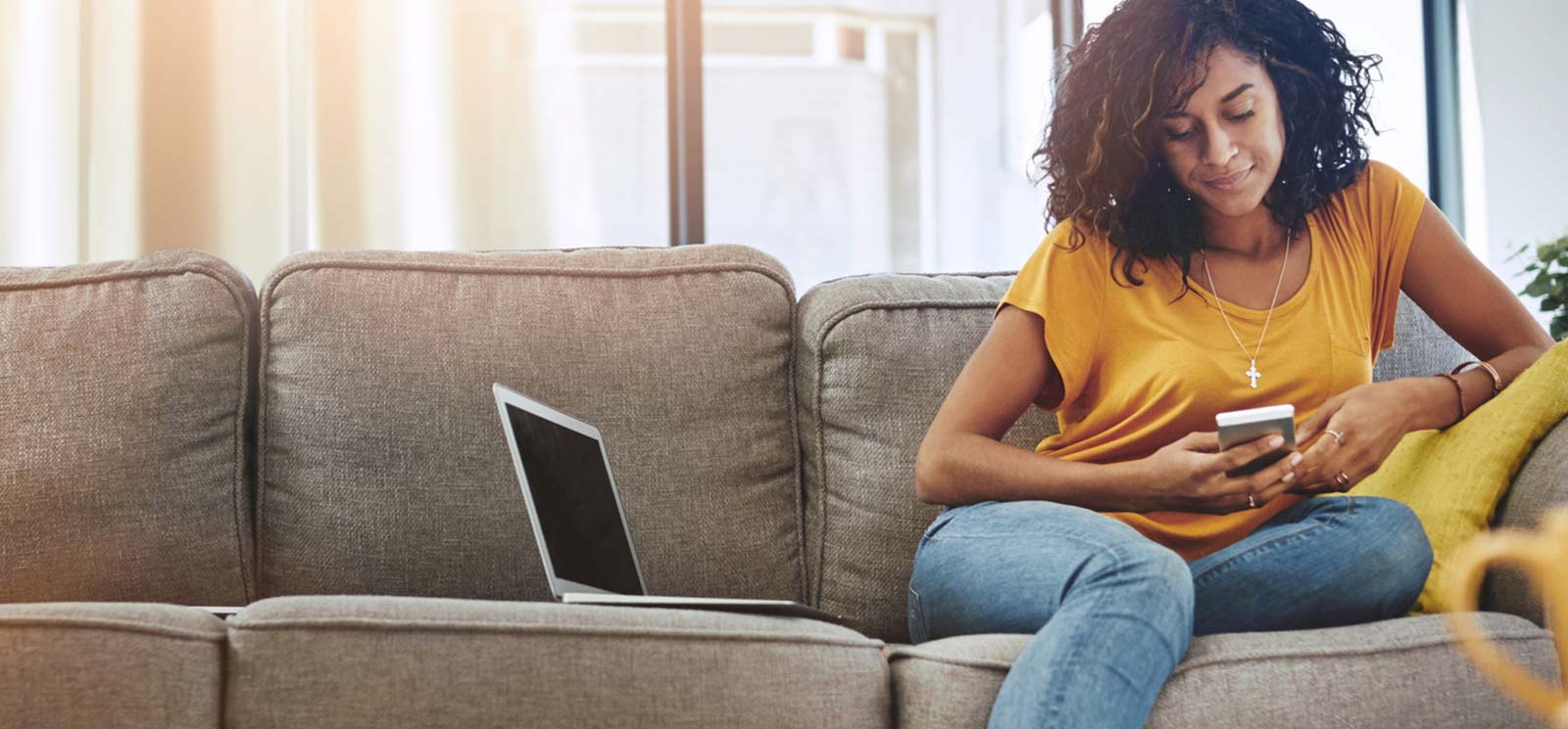 Person sitting on couch on phone next to laptop.